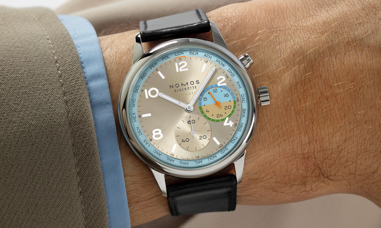 NOMOS Glashütte Club Sport neomatik Weltzeit Roam (Ref. 790.S10) mit champagnerfarbenem Zifferblatt am schwarzen Lederarmband an einem Handgelenk mit beigem Ärmel getragen