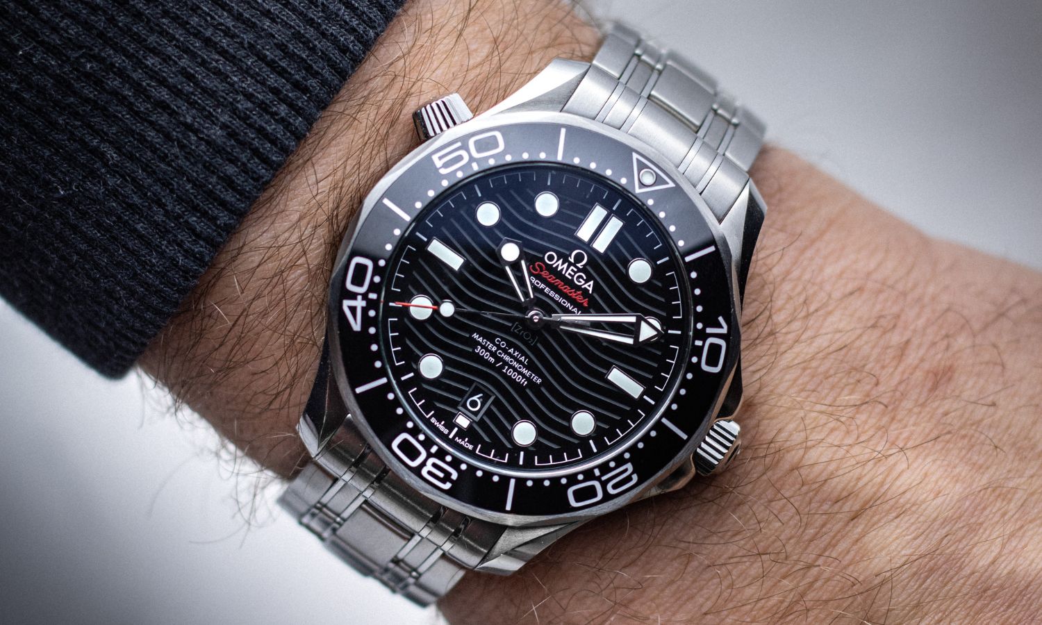 OMEGA Seamaster Diver 300M Referenz 210.30.42.20.01.001 mit schwarzem Zifferblatt am Edelstahlarmband an einem Handgelenk mit schwarzem Ärmel getragen