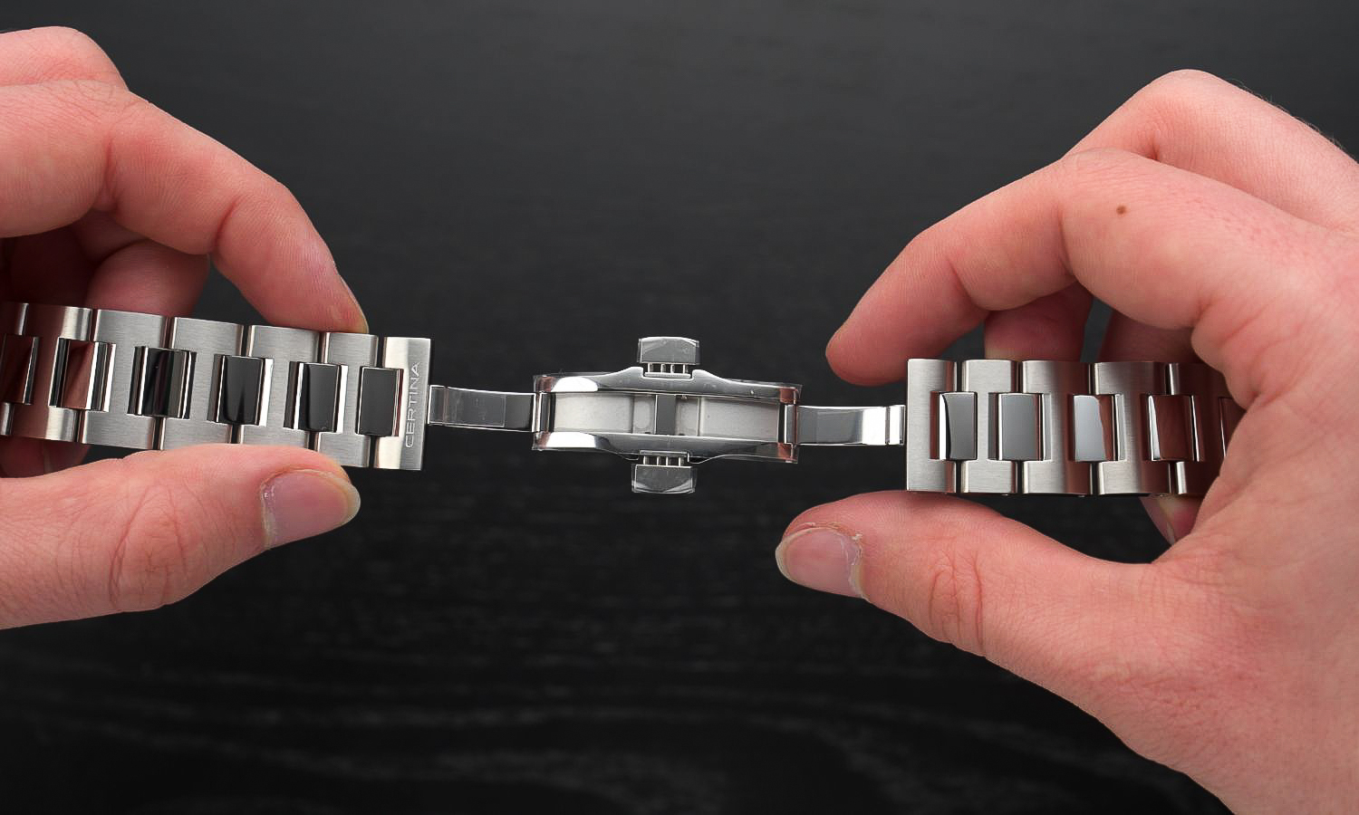 Das Edelstahlarmband und die geöffnete Schließe der Certina DS PH200M in zwei Händen gehalten abgebildet vor schwarzem Hintergrund