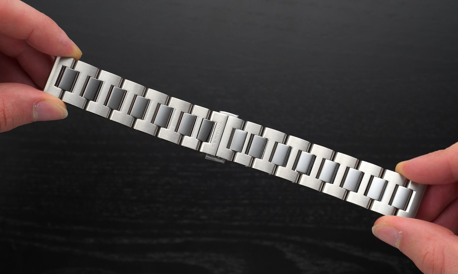 Das Edelstahlarmband der Certina DS PH200M in zwei Händen gehalten abgebildet vor schwarzem Hintergrund