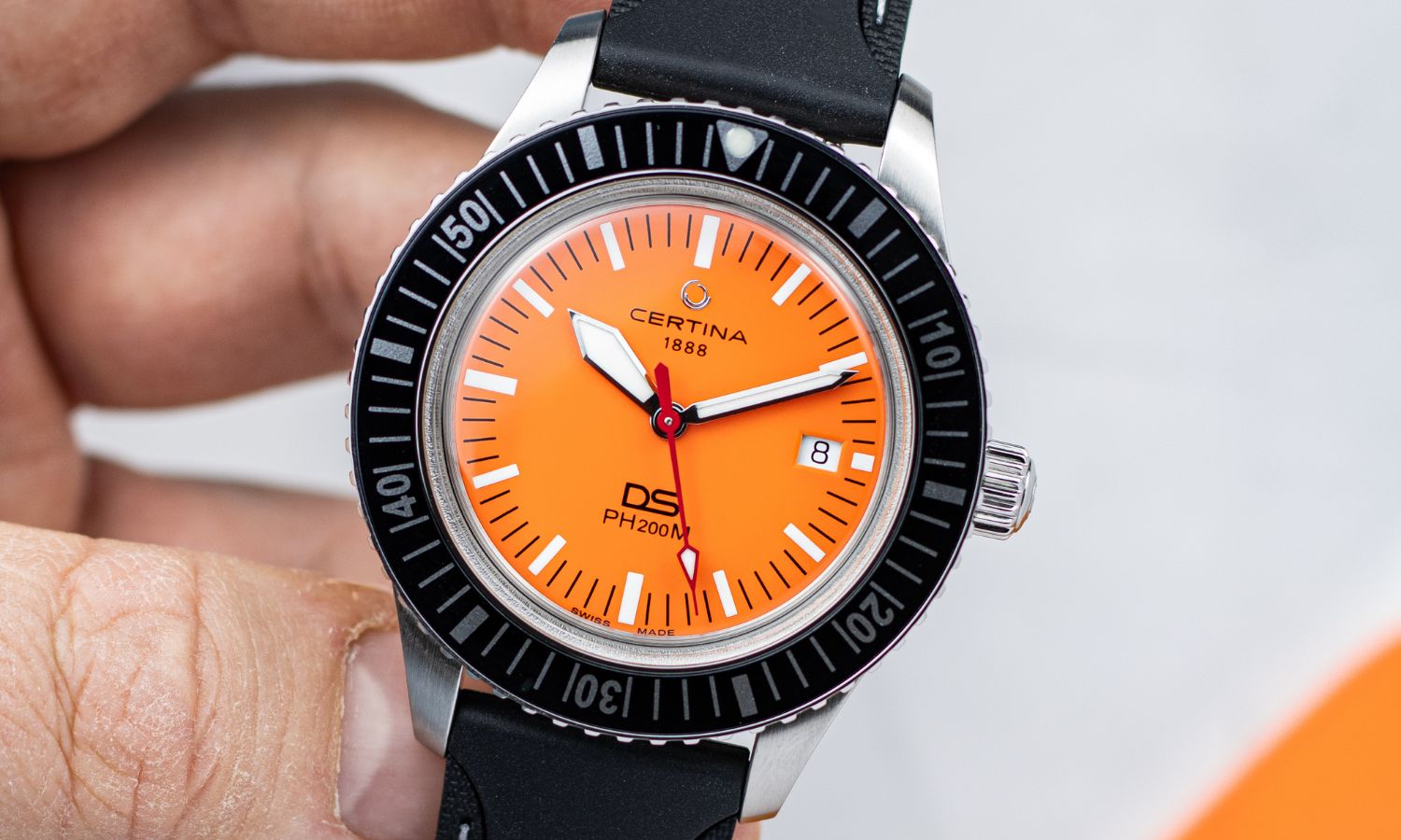 Certina DS PH200M Powermatic 80 mit orangenem Zifferblatt in einer Hand gehalten von vorne abgebildet vor hellgrauem Hintergrund