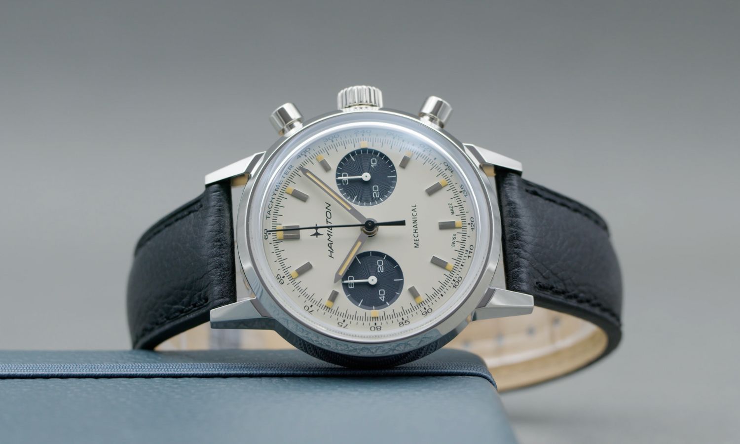 Der Hamilton Intra-Matic Handaufzug Chronograph mit silbernem Zifferblatt am schwarzen Lederarmband seitlich liegend vor grauem Hintergrund