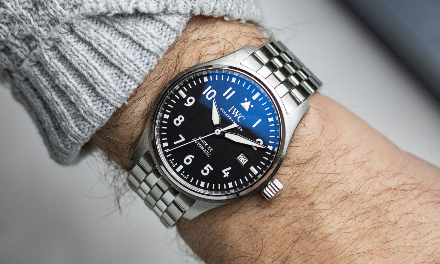 IWC Mark XX mit schwarzem Zifferblatt am Edelstahlarmband an einem Handgelenk mit grauem Ärmel getragen