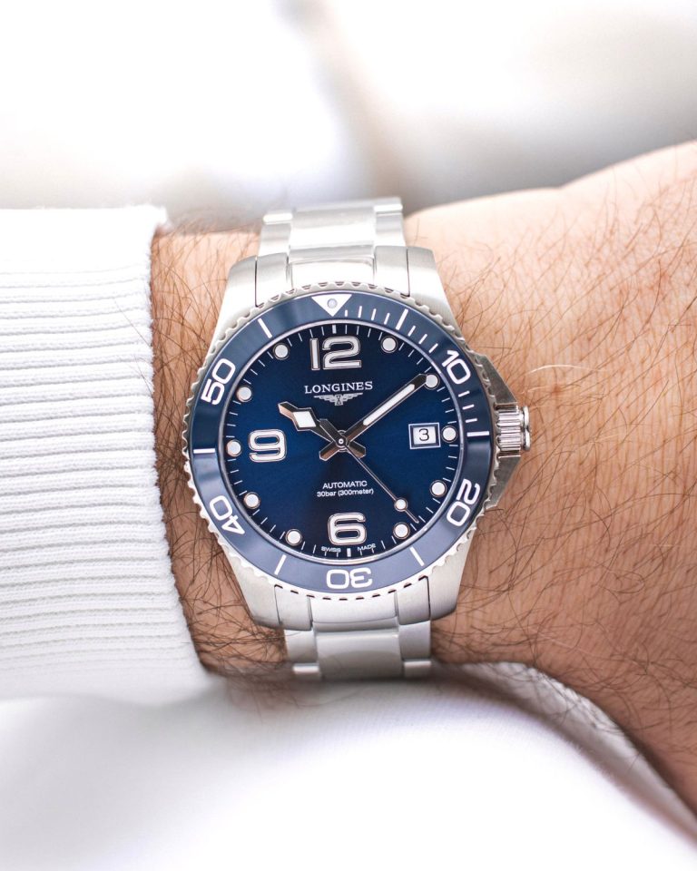 Longines HydroConquest mit dunkelblauem Zifferblatt am Edelstahlarmband an einem Handgelenk mit weißem Ärmel getragen vor weißem Hintergrund abgebildet
