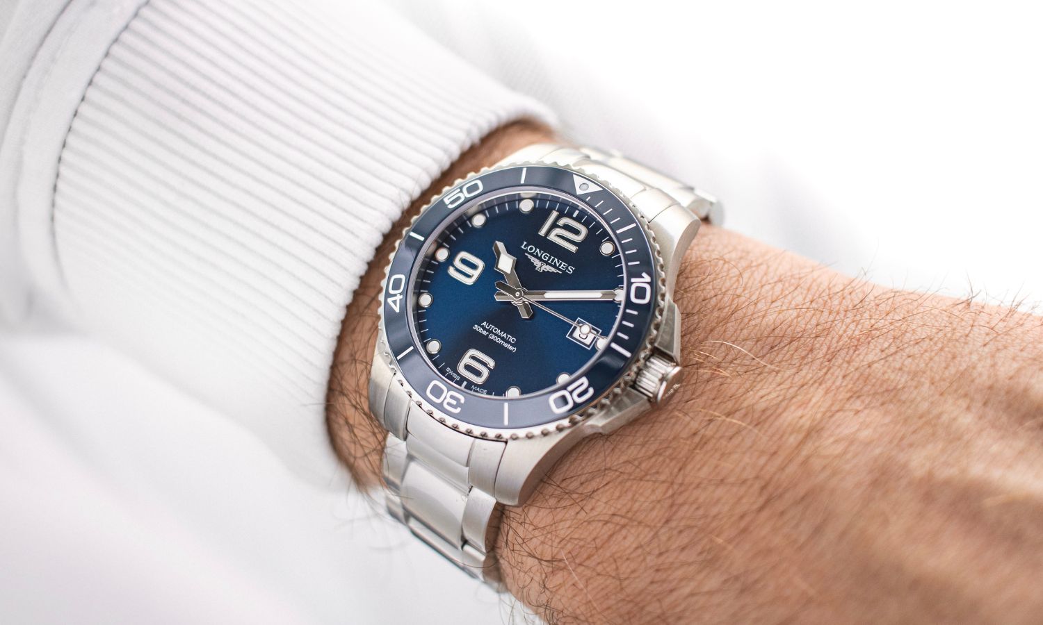 Longines HydroConquest mit dunkelblauem Zifferblatt am Edelstahlarmband an einem Handgelenk mit weißem Ärmel getragen vor weißem Hintergrund abgebildet