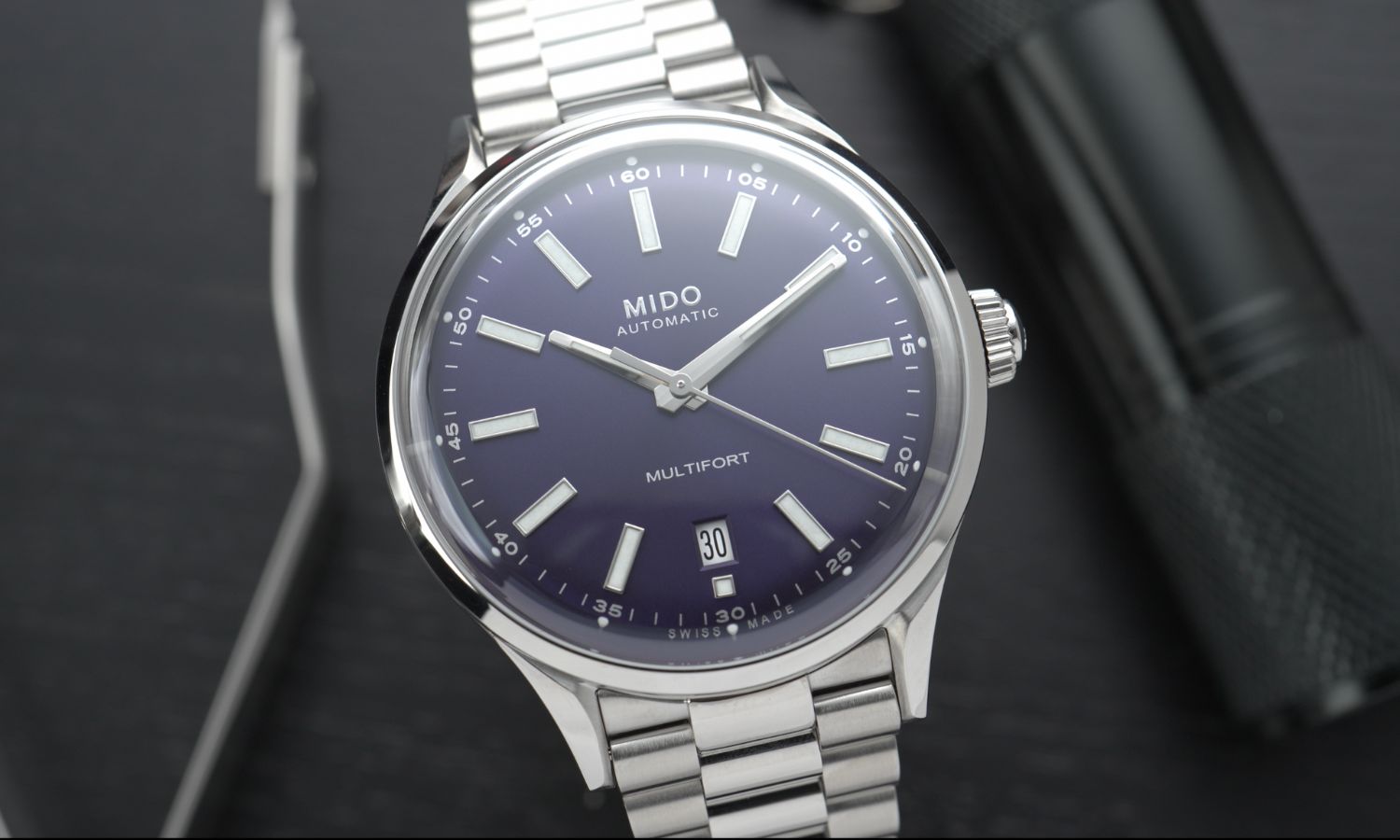 Nahaufnahme des dunkelblauen Zifferblatts der Mido Multifort Patrimony Powerwind am Edelstahlarmband stehend von vorne abgebildet vor schwarzem Hintergrund