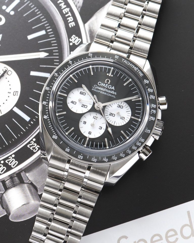 OMEGA Speedmaster Moonwatch Professional „Reverse Panda“ Referenz 310.30.42.50.01.004 mit schwarzem Zifferblatt am Edelstahlarmband auf einer Abbildung der Uhr aus einem Buch liegend