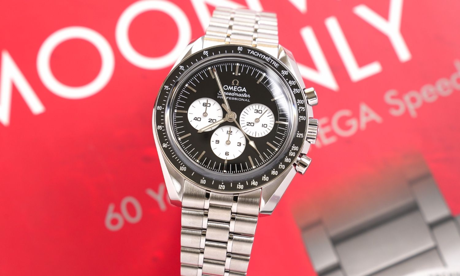 OMEGA Speedmaster Moonwatch Professional „Reverse Panda“ Referenz 310.30.42.50.01.004 mit schwarzem Zifferblatt am Edelstahlarmband abgebildet vor rotem Hintergrund