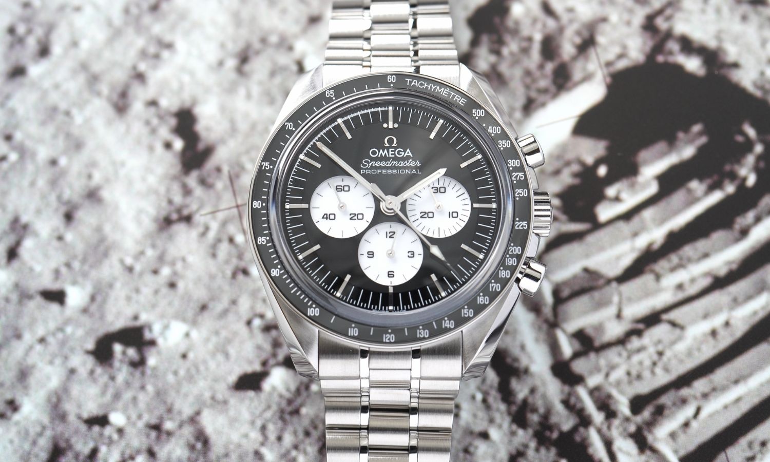 OMEGA Speedmaster Moonwatch Professional „Reverse Panda“ Referenz 310.30.42.50.01.004 mit schwarzem Zifferblatt am Edelstahlarmband abgebildet vor einem Mondoberflächen-Hintergrund