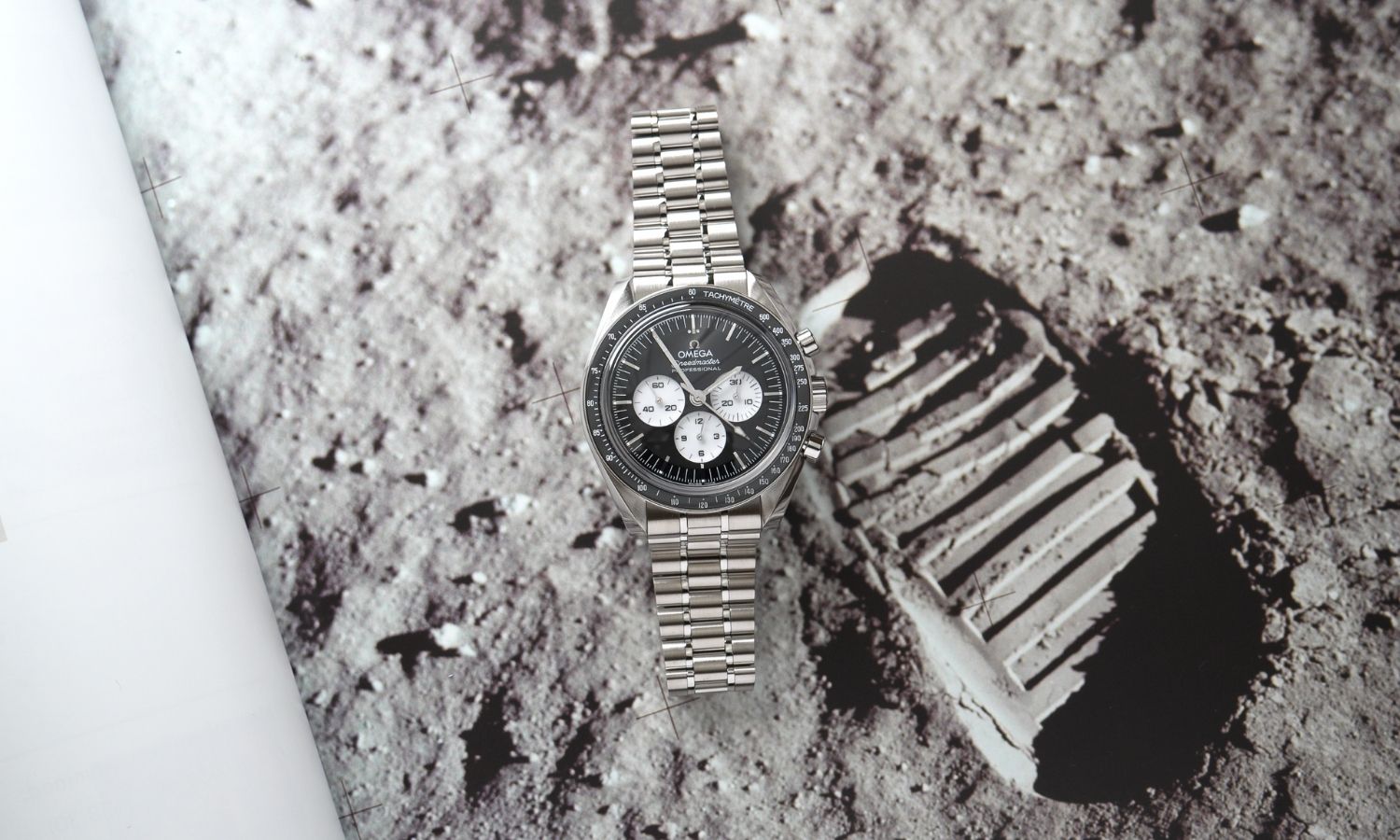 OMEGA Speedmaster Moonwatch Professional „Reverse Panda“ Referenz 310.30.42.50.01.004 mit schwarzem Zifferblatt am Edelstahlarmband abgebildet vor einem Mondoberflächen-Hintergrund