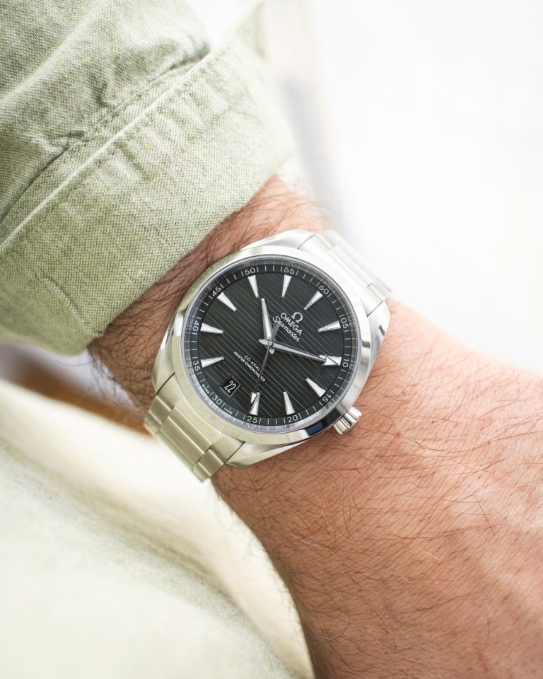 OMEGA Seamaster Aqua Terra 41 mit grünem Zifferblatt am Edelstahlarmband an einem Handgelenk mit grünem Ärmel getragen vor hellem Hintergrund