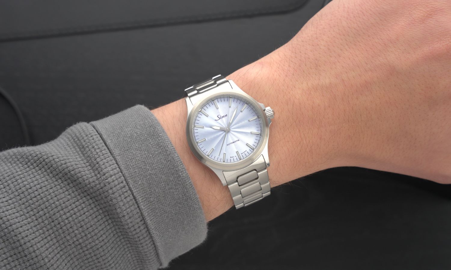 Sinn 556 H-Link mit eisblauem Zifferblatt an einem Handgelenk mit grauem Ärmel getragen vor schwarzem Hintergrund abgebildet