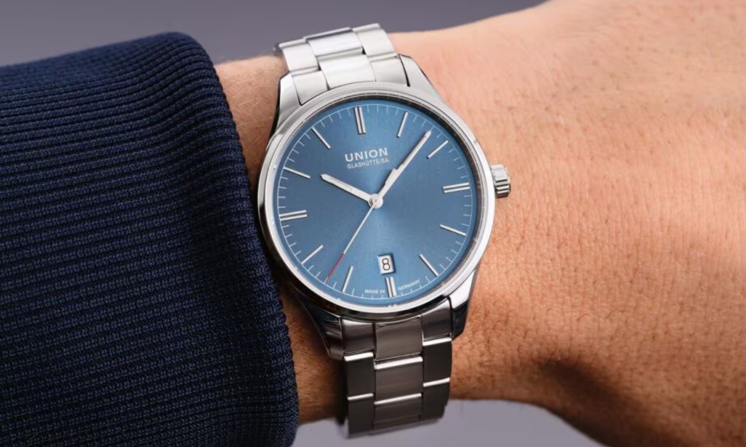 UNION Glashütte Viro Datum 39 mit blauem Zifferblatt am Edelstahlarmband an einem Handgelenk mit dunkelblauem Ärmel getragen