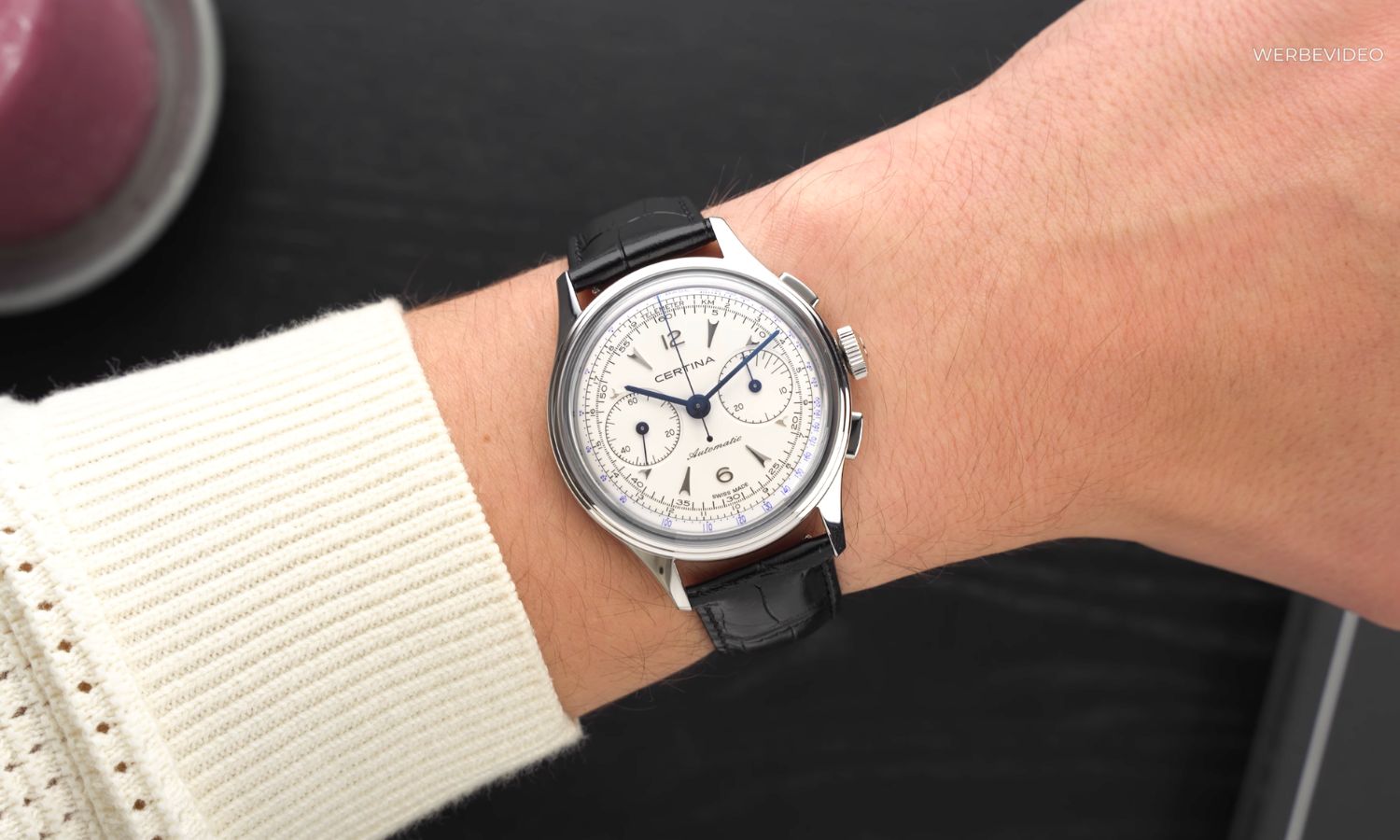 Certina DS Chronograph Automatic mit weißem Zifferblatt am schwarzen Lederarmband an einem Handgelenk mit weißem Ärmel getragen vor schwarzem Hintergrund abgebildet
