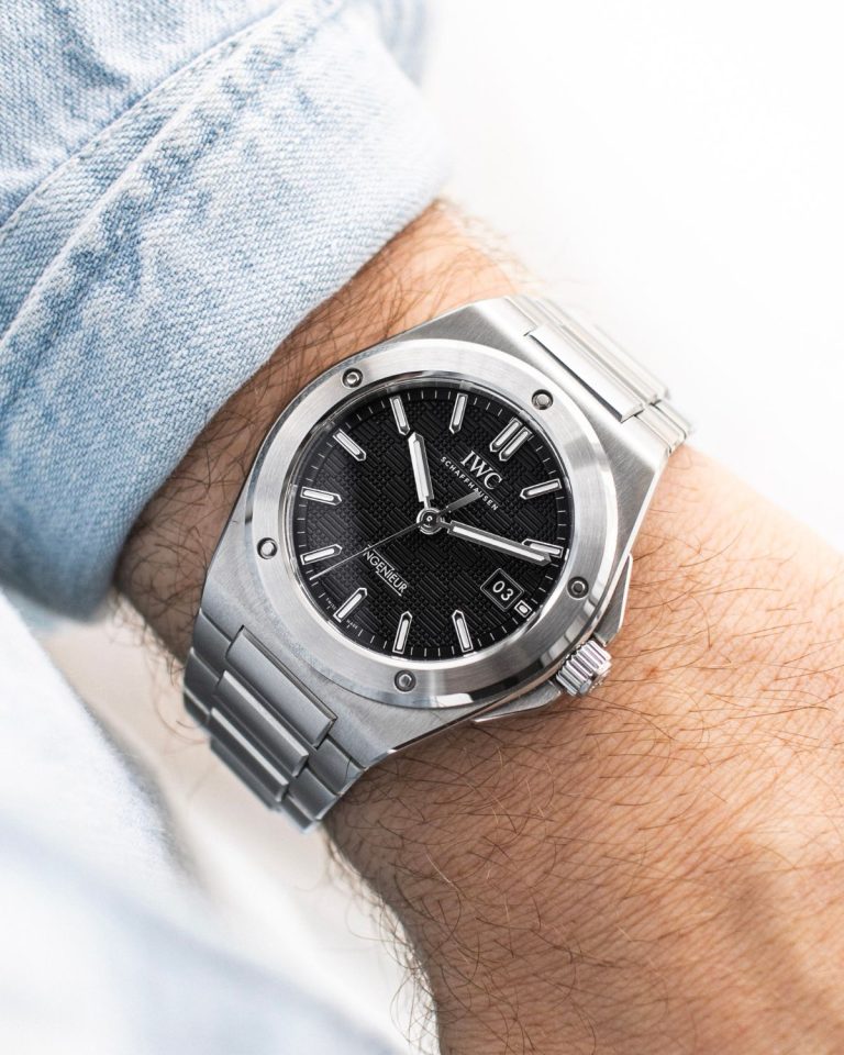 IWC Ingenieur Automatic 40 mit schwarzem Zifferblatt am Edelstahlarmband an einem Handgelenk mit hellblauem Ärmel getragen vor weißem Hintergrund