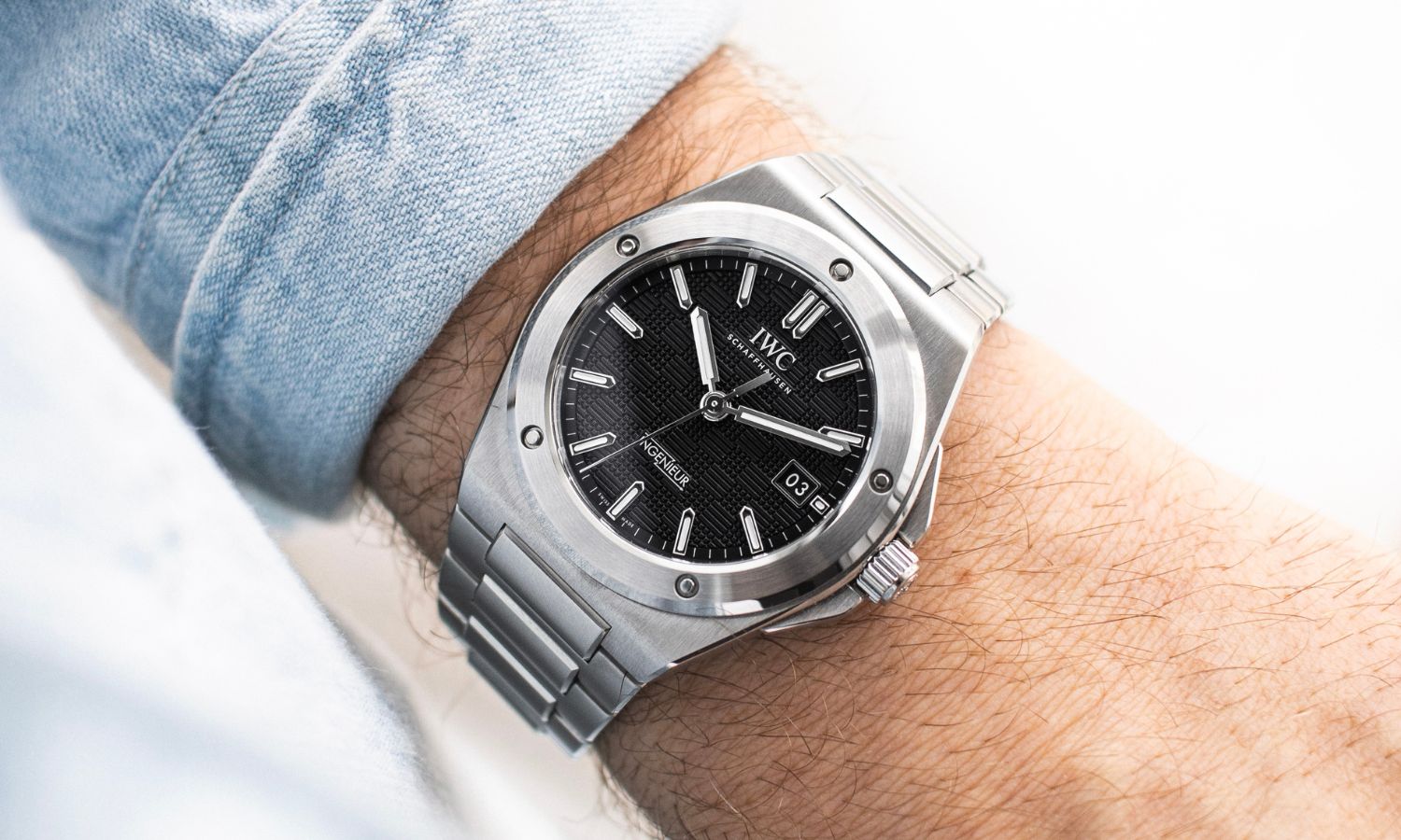 IWC Ingenieur Automatic 40 mit schwarzem Zifferblatt am Edelstahlarmband an einem Handgelenk mit hellblauem Ärmel getragen vor weißem Hintergrund