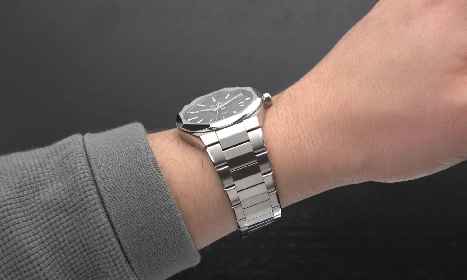 Das Edelstahlband der Mido Multifort 8 One Crown an einem Handgelenk mit grauem Ärmel getragen vor schwarzem Hintergrund