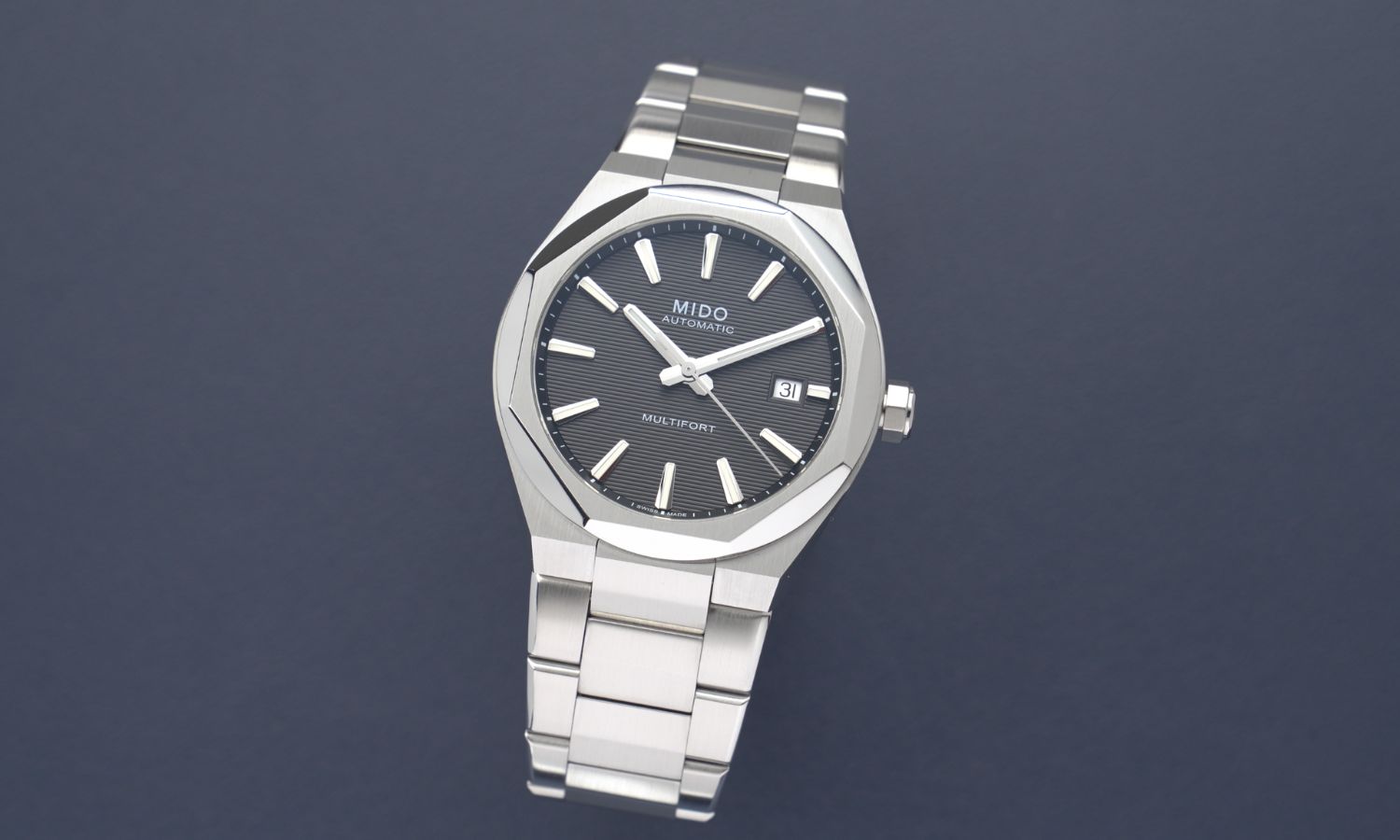 Mido Multifort 8 One Crown Referenz M055.507.11.051.00 mit schwarzem Zifferblatt am Edelstahlband stehend vor dunkelblauem Hintergrund