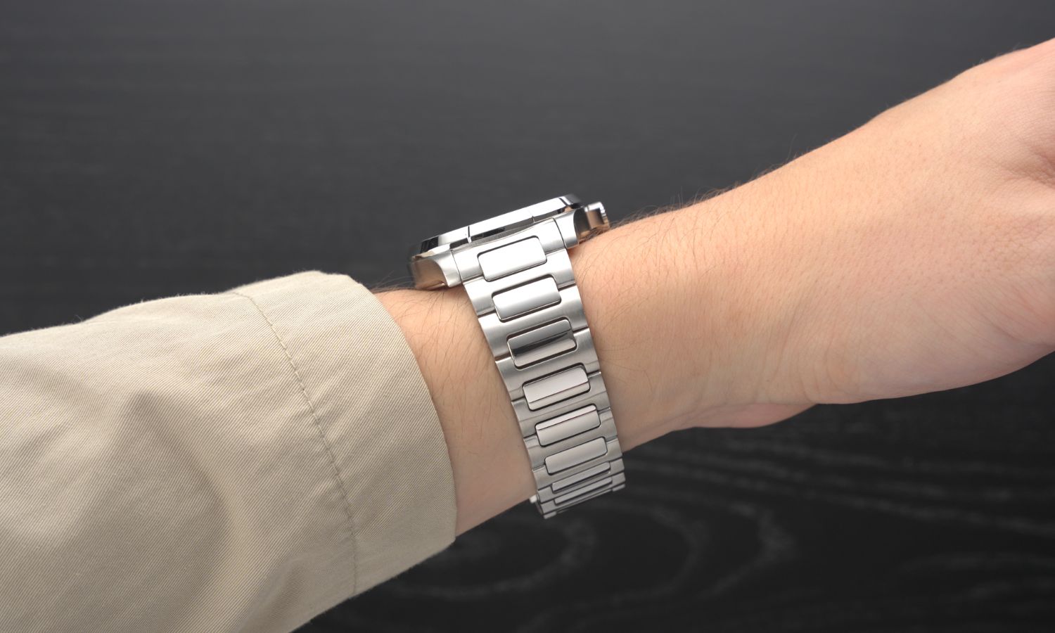 Das Edelstahlband der Mido Multifort TV Big Date an einem Handgelenk mit beigem Ärmel getragen vor schwarzem Hintergrund