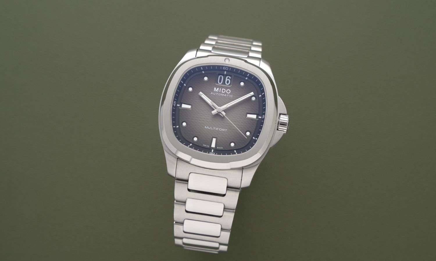 Mido Multifort TV Big Date Referenz M049.526.11.081.00 mit schwarzem Zifferblatt am Edelstahlband stehend vor dunkelgrünem Hintergrund