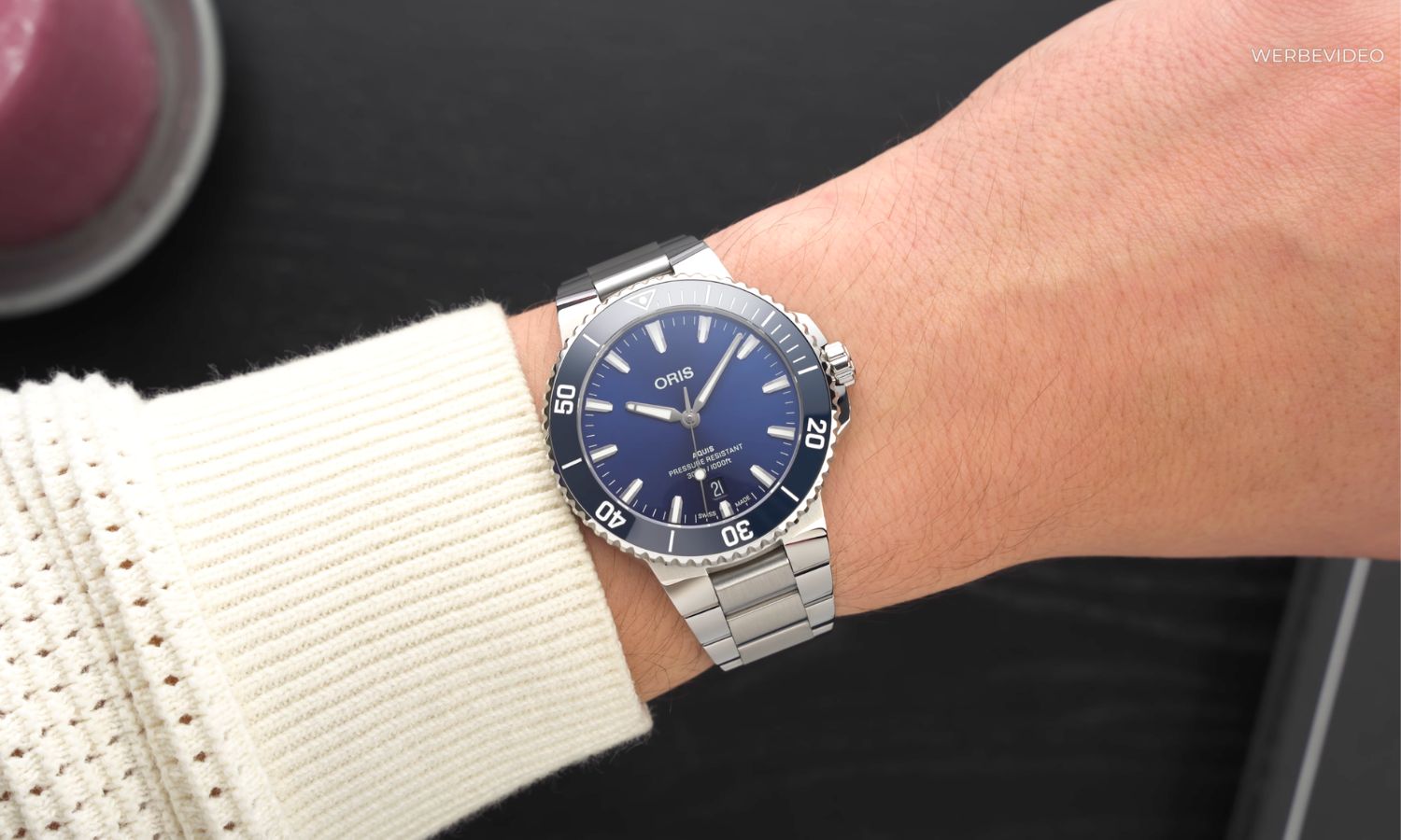 Oris Aquis Date Blau 41,5 mit dunkelblauem Zifferblatt am Edelstahlarmband an einem Handgelenk mit weißem Ärmel getragen vor schwarzem Hintergrund abgebildet