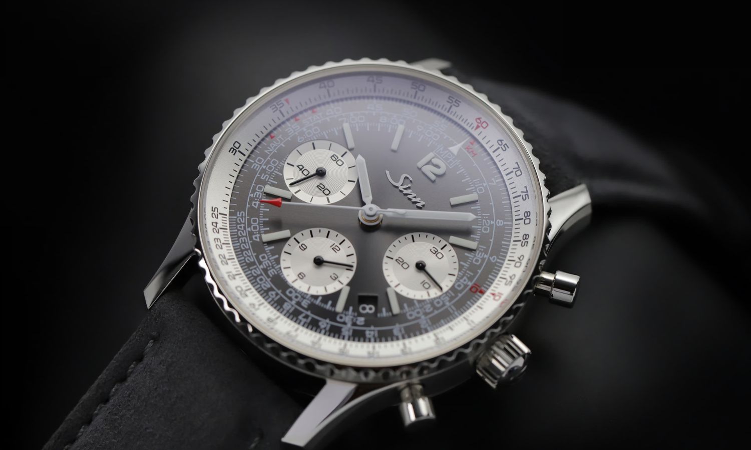 Sinn 903 St II A mit anthrazitfarbenem Zifferblatt am schwarzen Lederarmband liegend auf schwarzem Untergrund