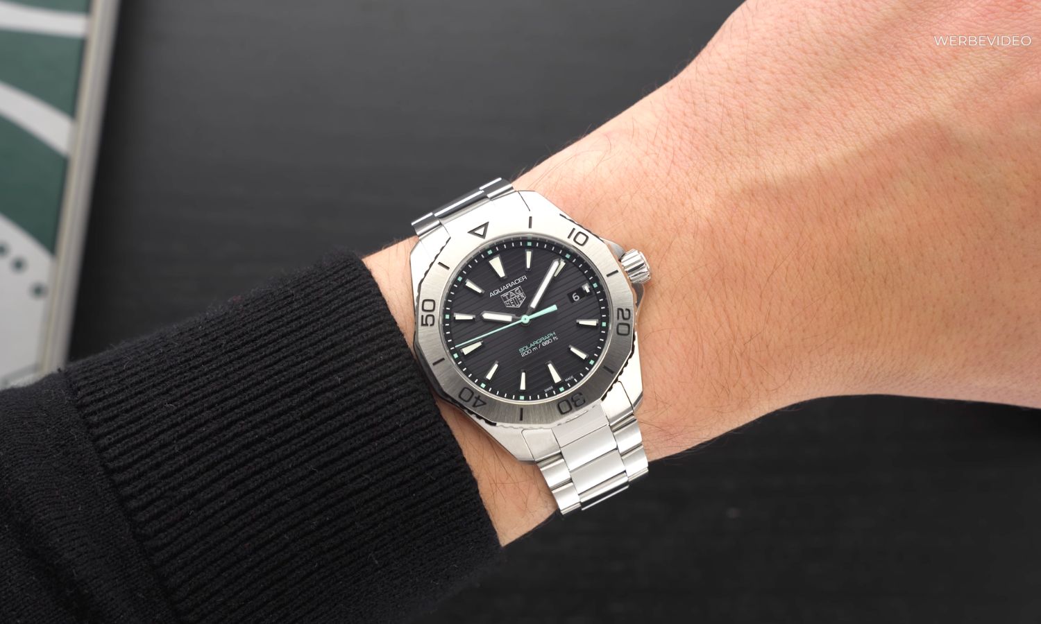 TAG HEUER Aquaracer Professional 200 Solagraph mit schwarzem Zifferblatt am Edelstahlarmband an einem Handgelenk mit schwarzem Ärmel getragen vor schwarzem Hintergrund abgebildet