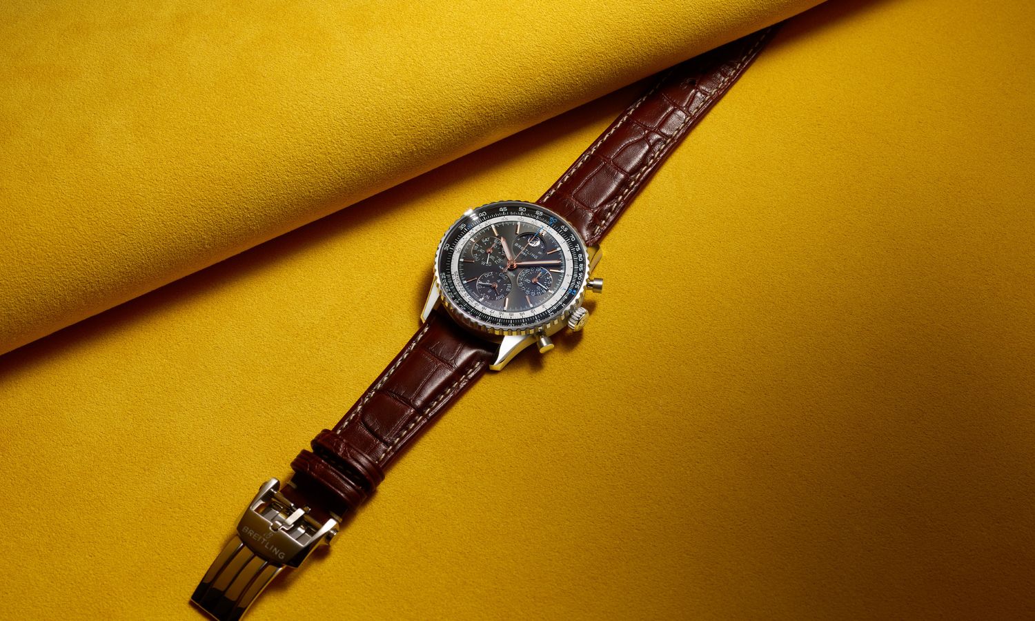 Breitling Navitimer B19 Chronograph 43 Perpetual Calendar mit anthrazitfarbenem Zifferblatt am braunen Lederarmband liegend auf gelbem Untergrund