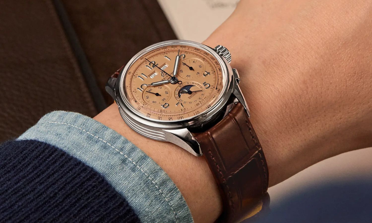 Breitling Premier B25 Datora 42 mit lachsfarbenem Zifferblatt am braunen Lederarmband an einem Handgelenk mit dunkelblauem Ärmel getragen