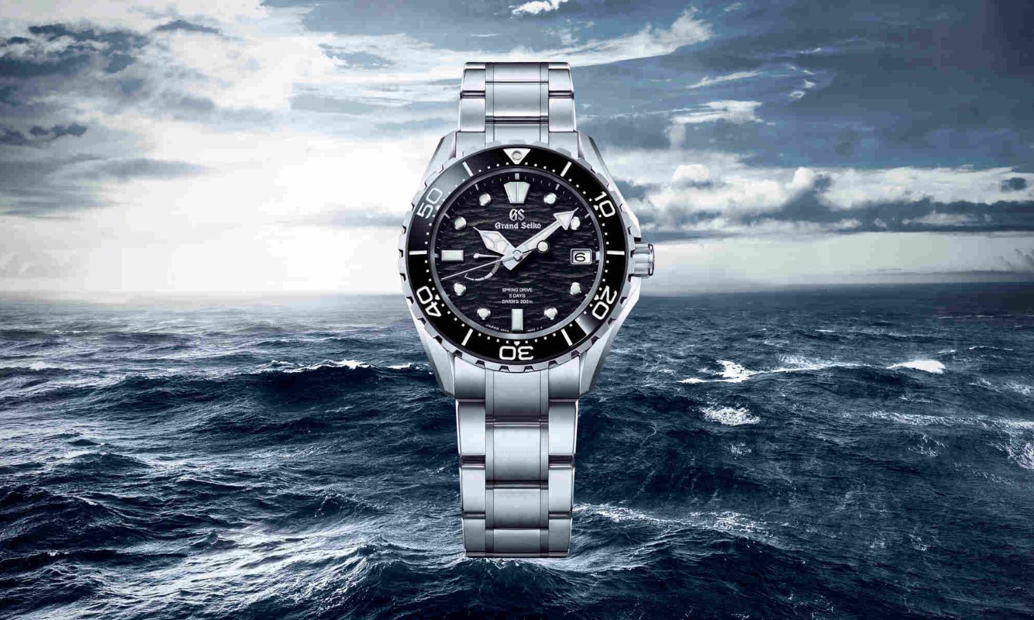 Grand Seiko Evolution 9 Spring Drive SLGA015 mit schwarzem Zifferblatt am Edelstahlarmband vor einem Meer mit Wellen und einem blau weißen Himmel abgebildet