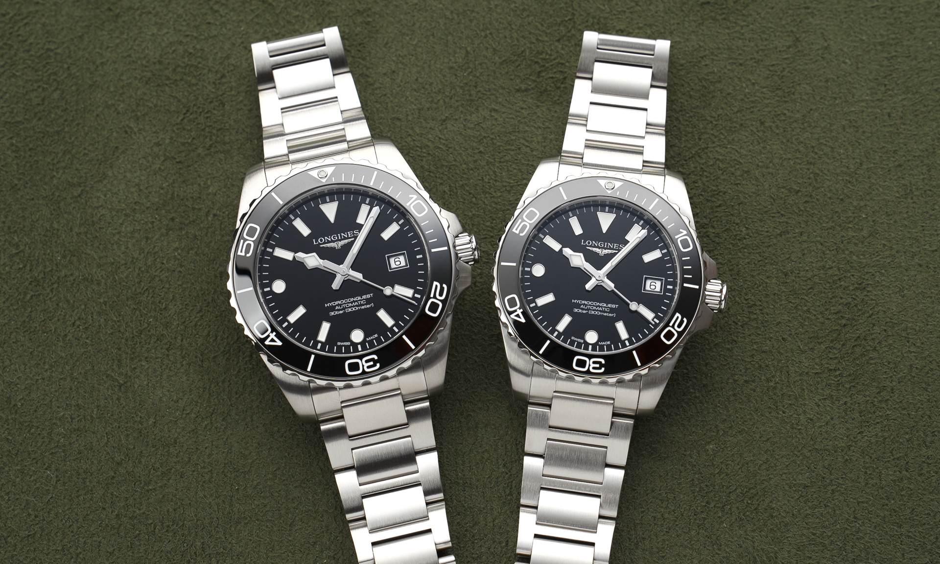 Longines HydroConquest 2026 mit schwarzem Zifferblatt am Edelstahlarmband in 42mm links und 39mm rechts nebeneinander liegend auf dunkelgrünem Untergrund von vorne abgebildet