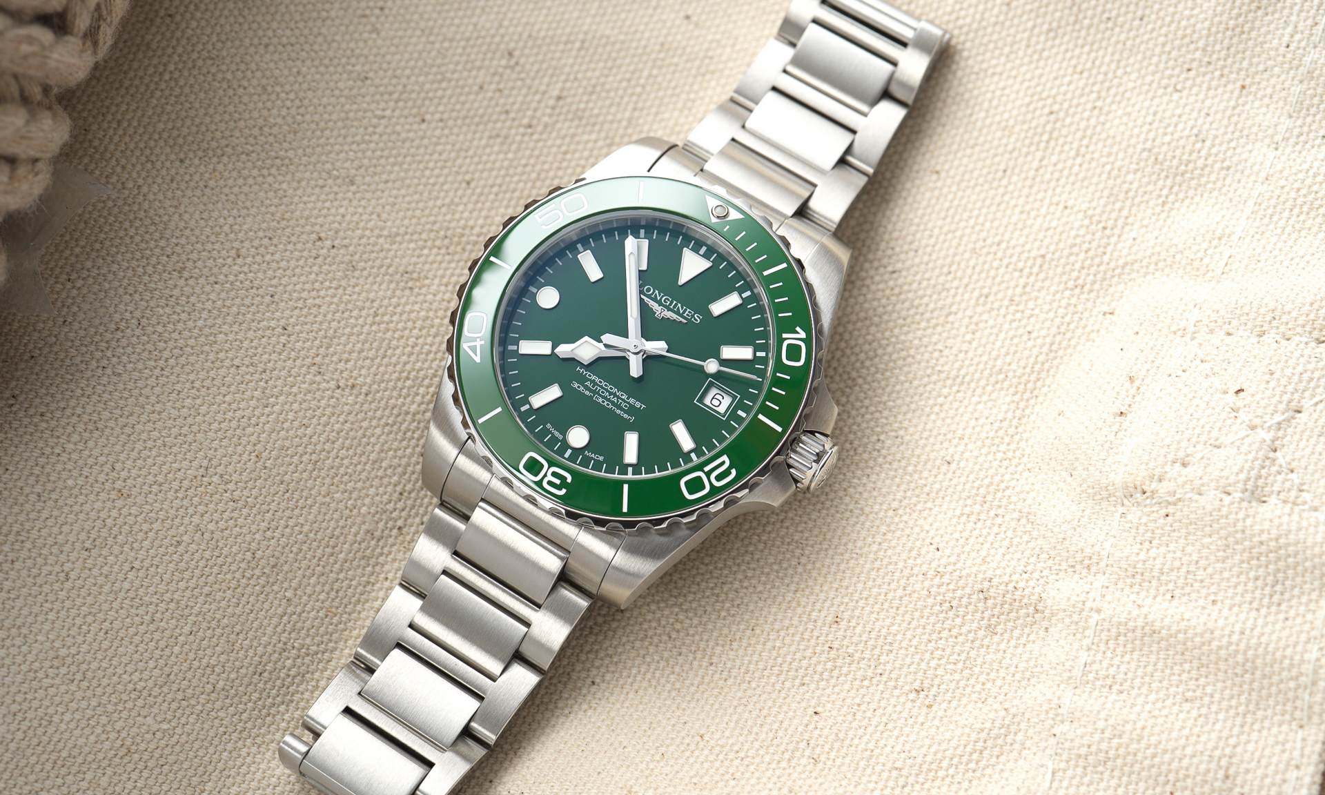 Longines HydroConquest 2026 mit grünem Zifferblatt am Edelstahlarmband liegend auf beigem Untergrund von vorne abgebildet