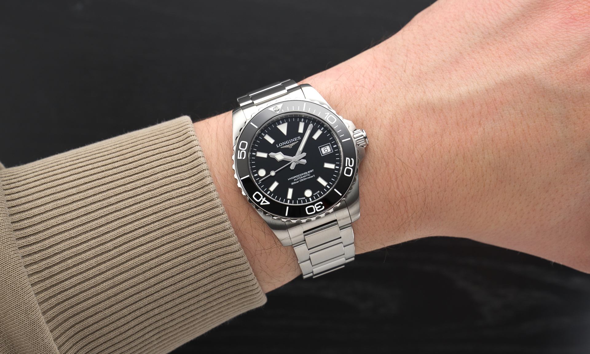 Longines HydroConquest 2026 mit schwarzem Zifferblatt am Edelstahlarmband an einem Handgelenk mit beigem Ärmel getragen vor schwarzem Hintergrund abgebildet