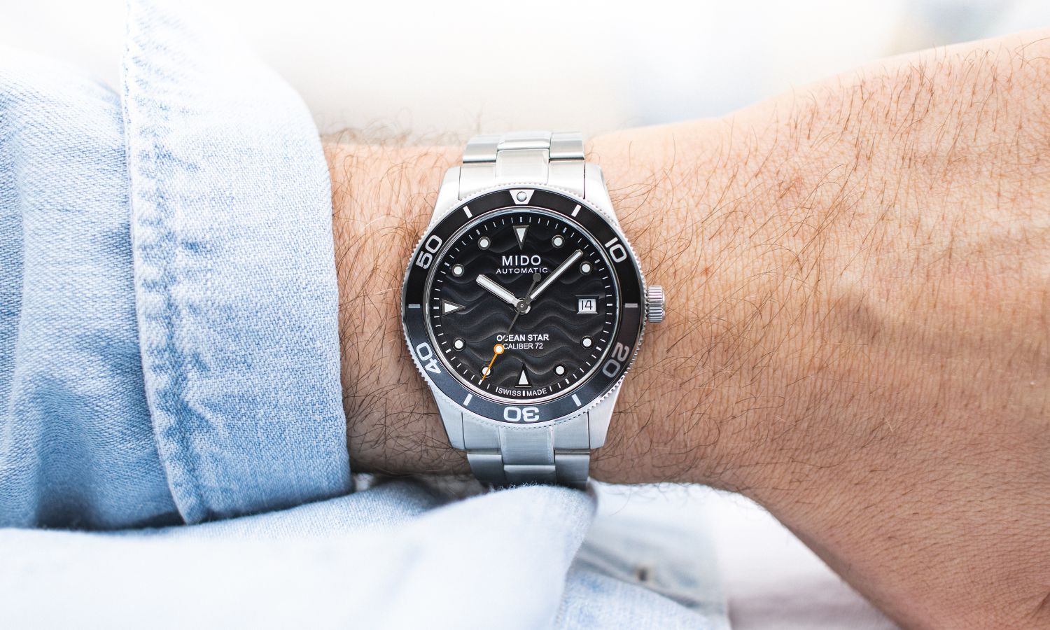 Mido Ocean Star 39 mit grauem Zifferblatt am Edelstahlarmband an einem Handgelenk mit hellblauem Ärmel getragen vor hellem Hintergrund abgebildet