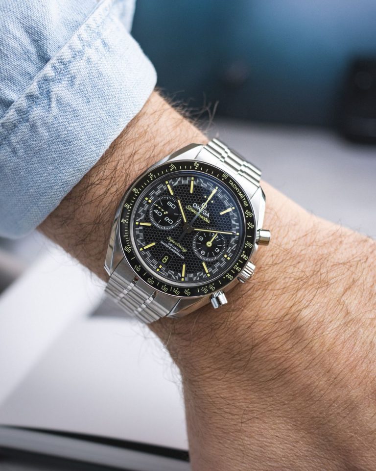 OMEGA Speedmaster Super Racing mit schwarzem Zifferblatt am Edelstahlarmband an einem Handgelenk mit hellblauem Ärmel getragen