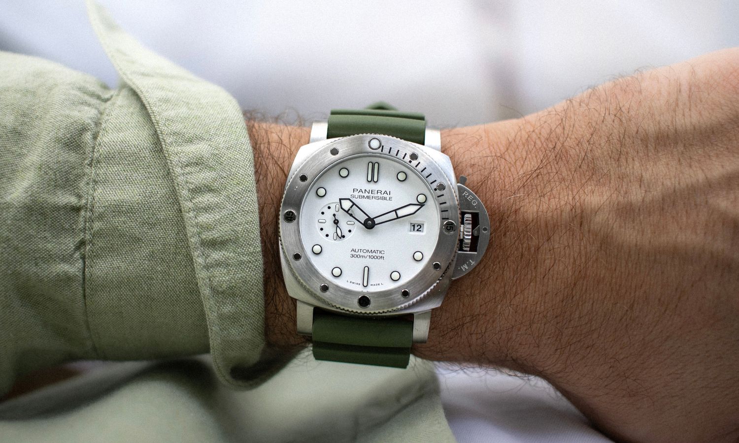 Panerai Submersible QuarantaQuattro Bianco mit weißem Zifferblatt am grünen Kautschukarmband an einem Handgelenk mit grünem Ärmel getragen vor hellem Hintergrund abgebildet