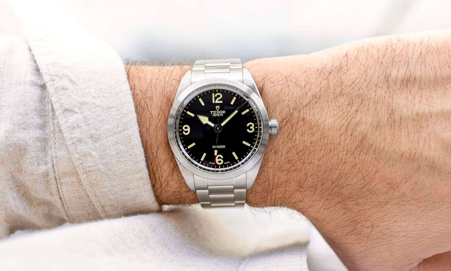 TUDOR Ranger 39 mit schwarzem Zifferblatt am Edelstahlarmband an einem Handgelenk mit beigem Ärmel getragen vor hellem Hintergrund abgebildet