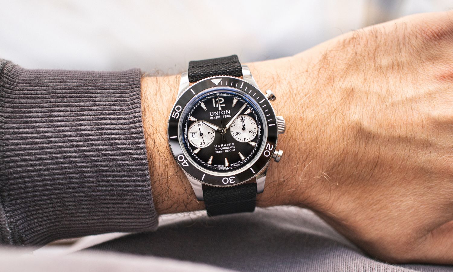 Union Glashütte Noramis Chronograph Sport mit schwarzem Zifferblatt am schwarzen Textilarmband an einem Handgelenk mit grauem Ärmel getragen