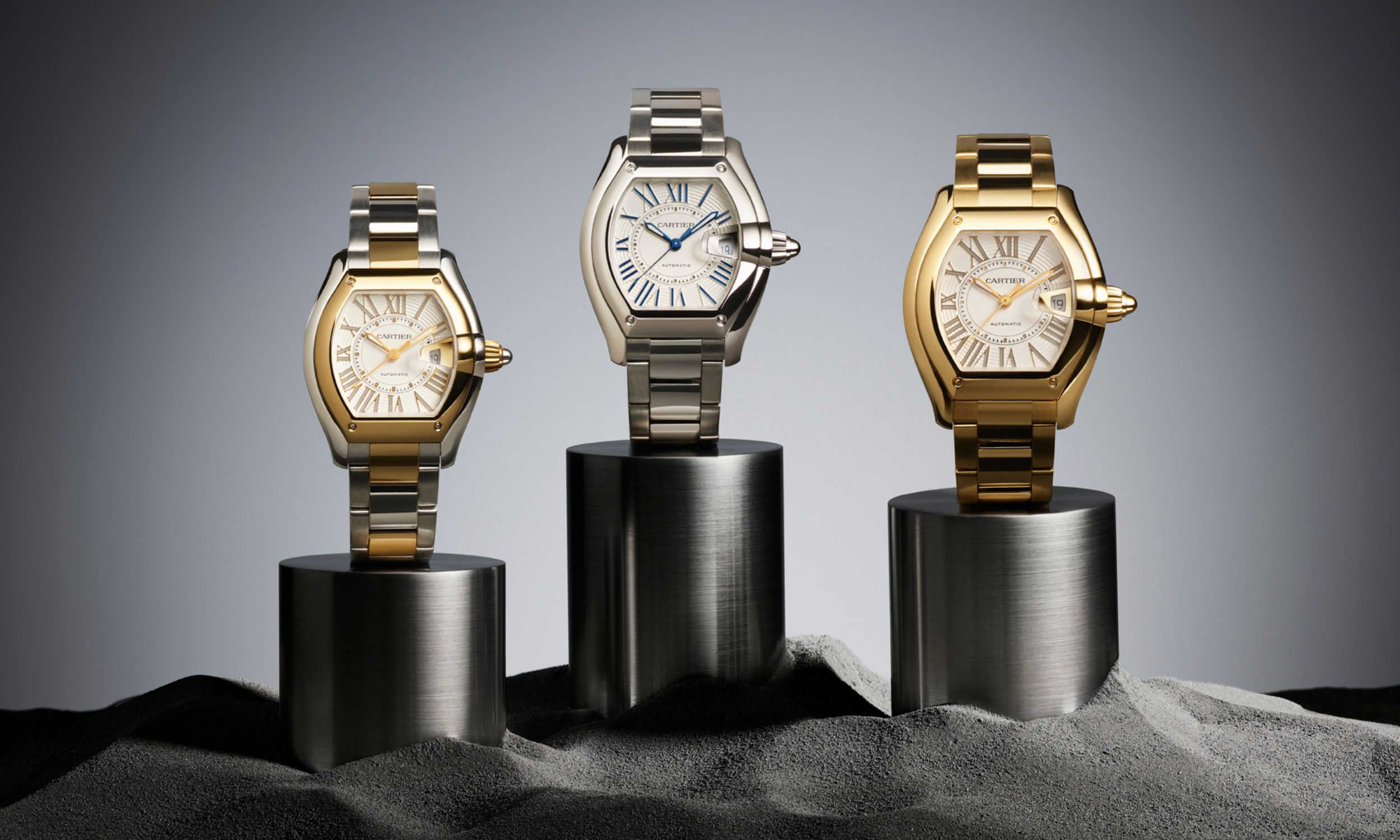 Drei Modelle der Cartier Roadster in verschiednen Gold-Ausführungen auf Sockeln stehend