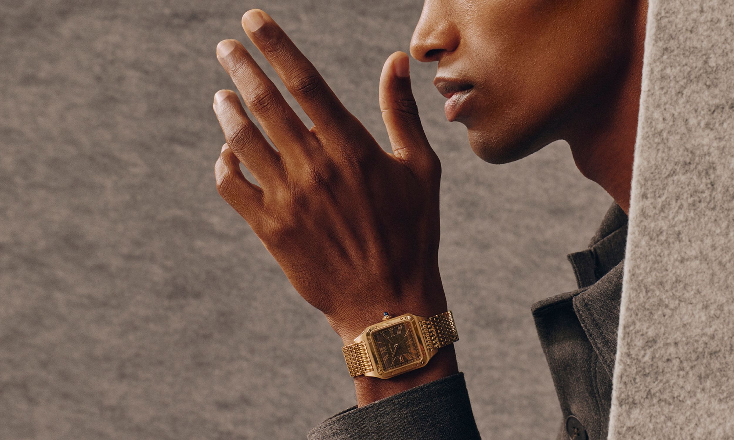 Scharze Frau trägt goldene Cartier Santos-Dumont mit braunem Zifferblatt am Handgelenk