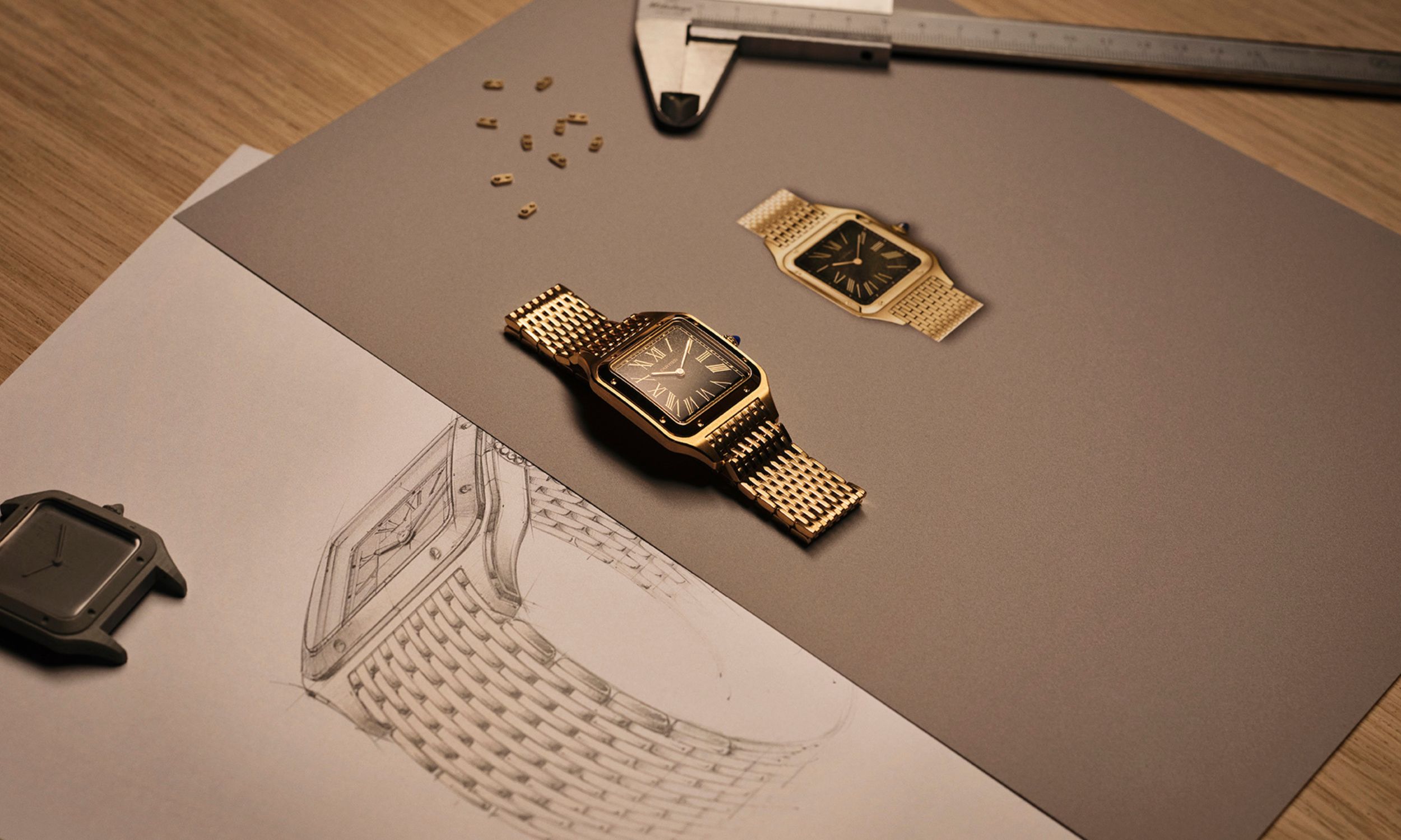 Goldene Cartier Santos-Dumont am Edelmetallarmband auf Buch mit technischen Zeichnungen der Uhr