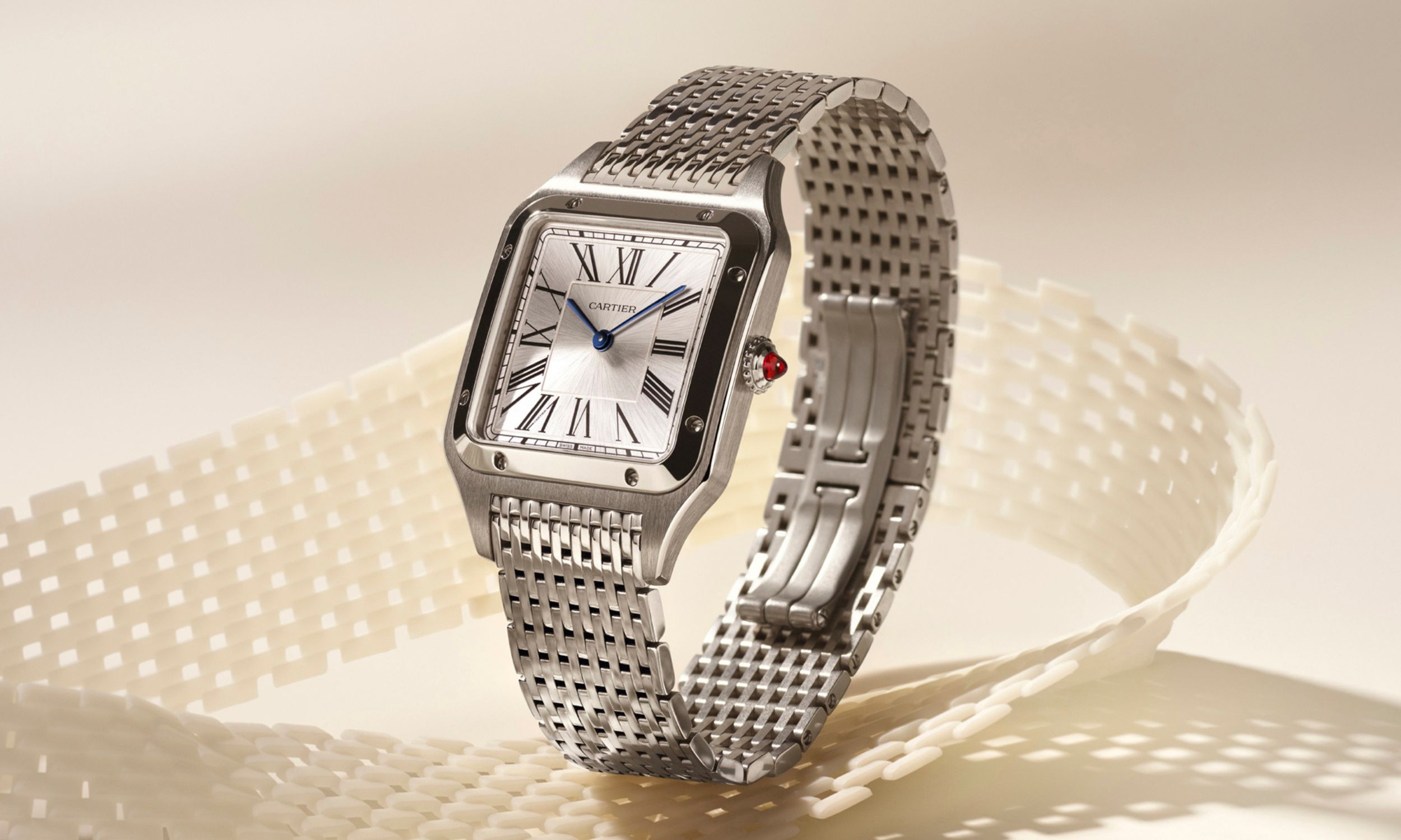 Stehende Cartier Santos-Dumont am Stahlarmband aus der Schrägansicht von rechts auf beigem Hintergrund mit Schleife