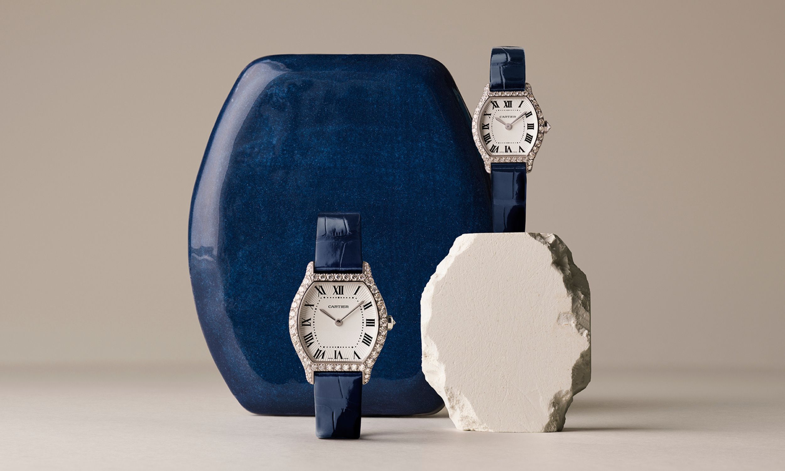 Zwei diamantbesetzte Cartier Tortue. Eine steht auf einem steinernen Sockel, die andere vor einer blauen Box