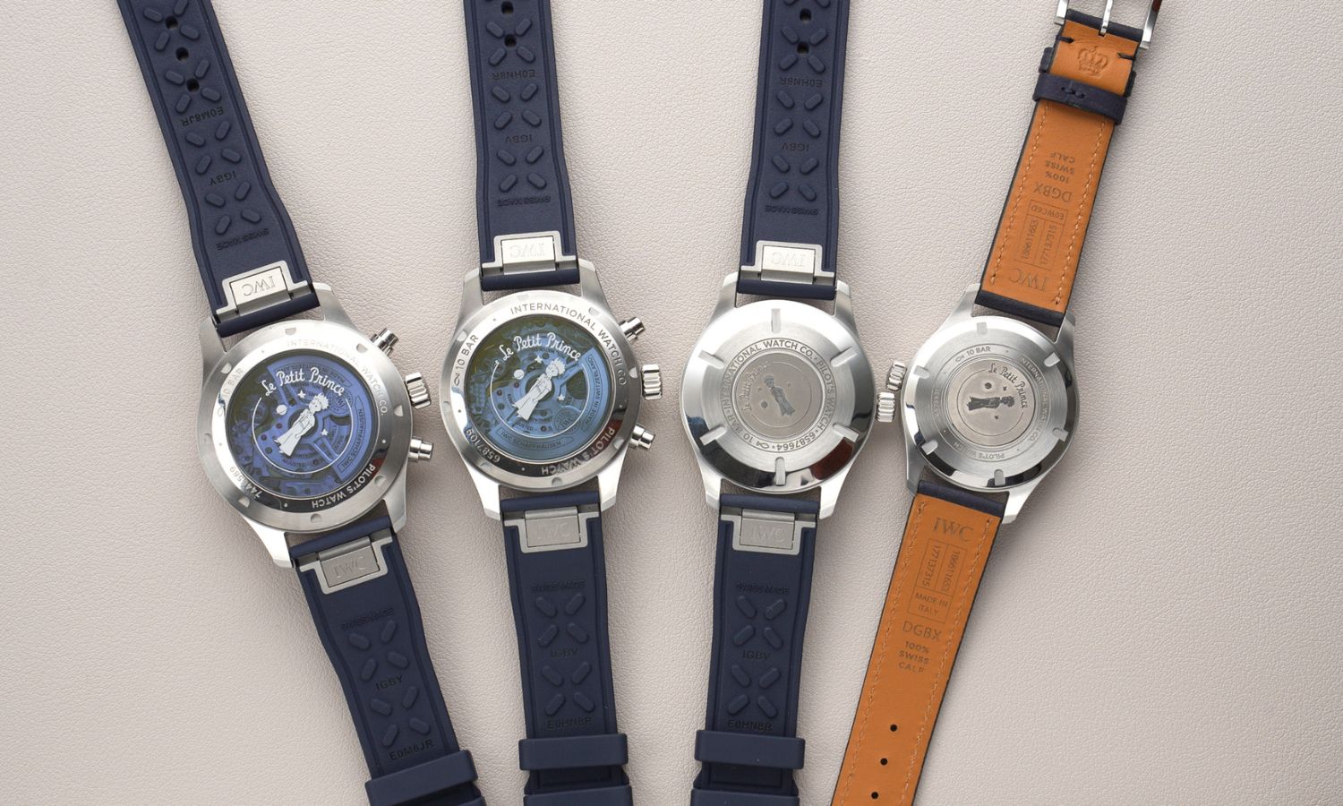 4 Modelle der IWC Le Petit Prince 20 Jahre Jubiläums-Edition nebeneinander liegend auf grauem Untergrund von hinten abgebildet