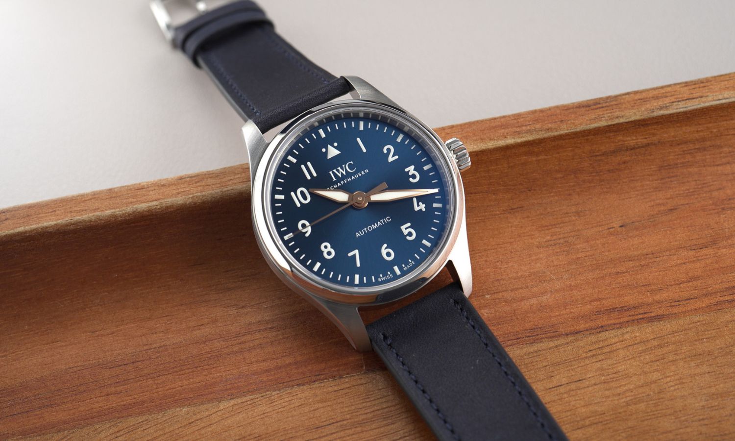 IWC Pilot's Watch 36 Le Petit Prince IW458802 mit dunkelblauem Zifferblatt am dunkelblauen Gummiband liegend auf hölzernem Untergrund