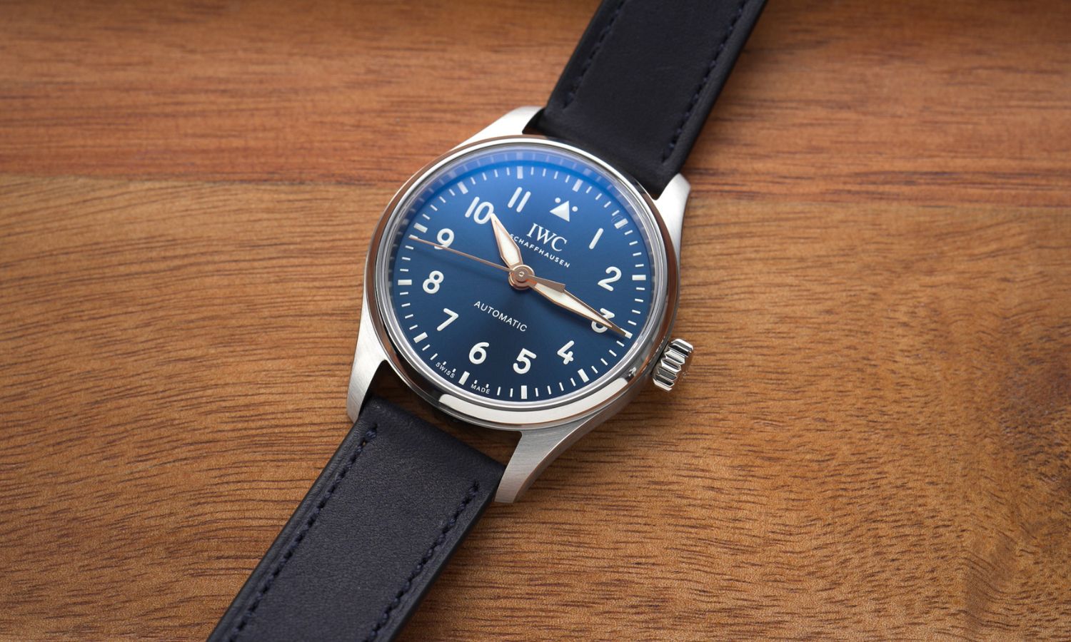 IWC Pilot's Watch 36 Le Petit Prince IW458802 mit dunkelblauem Zifferblatt am dunkelblauen Gummiband liegend auf hölzernem Untergrund