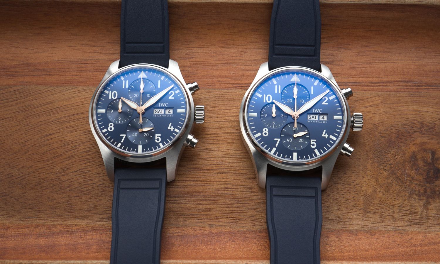 IWC Pilot's Watch Chronograph 41 Le Petit Prince IW388120 links und IWC Pilot's Watch Chronograph 43 Le Petit Prince IW378011 rechts mit blauen Zifferblättern an blauen Gummibändern nebeneinander liegend auf hölzernem Untergrund