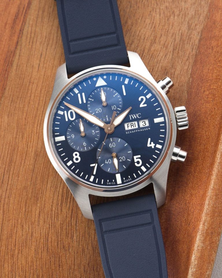 IWC Pilot's Watch Chronograph 41 Le Petit Prince IW388120 mit dunkelblauem Zifferblatt am dunkelblauen Gummiband liegend auf hölzernem Untergrund