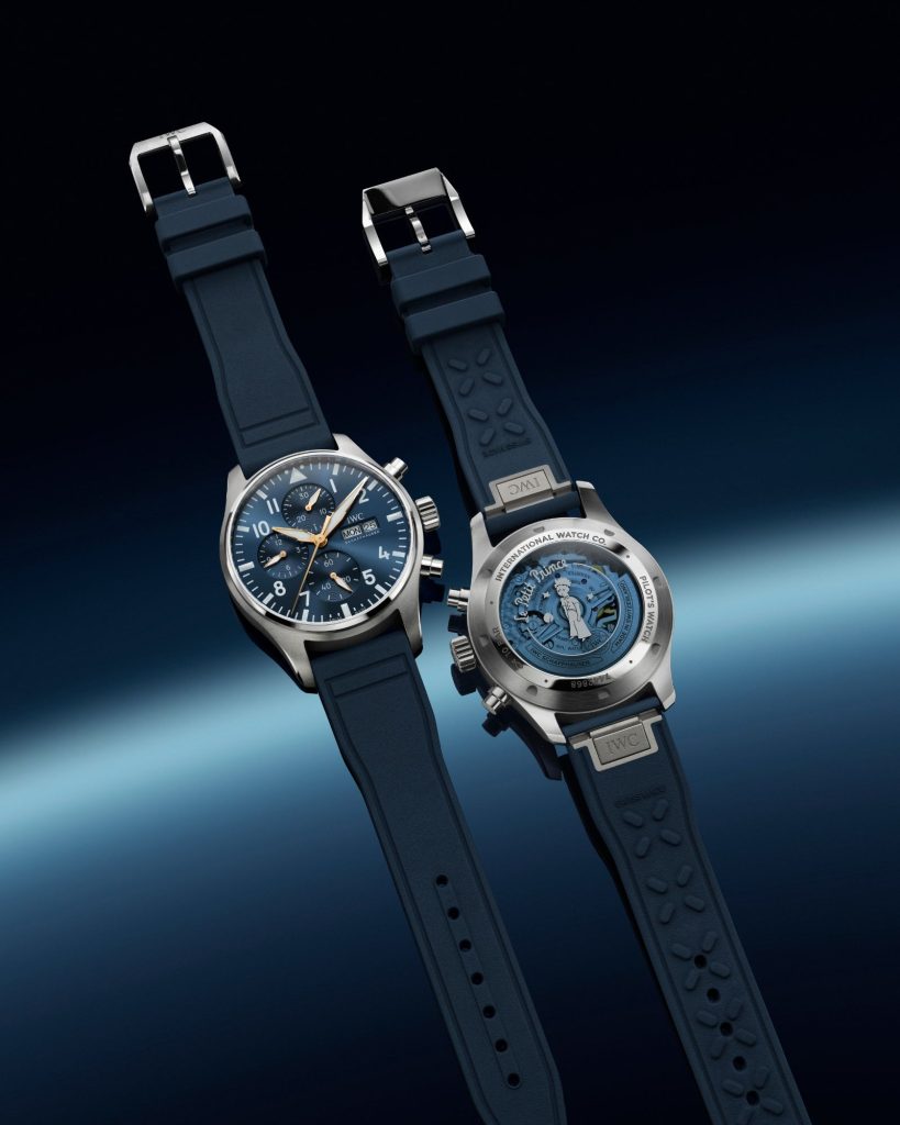 IWC Pilot's Watch Chronograph Le Petit Prince mit dunkelblauem Zifferblatt am blauen Kautschukarmband liegend von vorne und von hinten abgebildet vor dunkelblauem Hintergrund