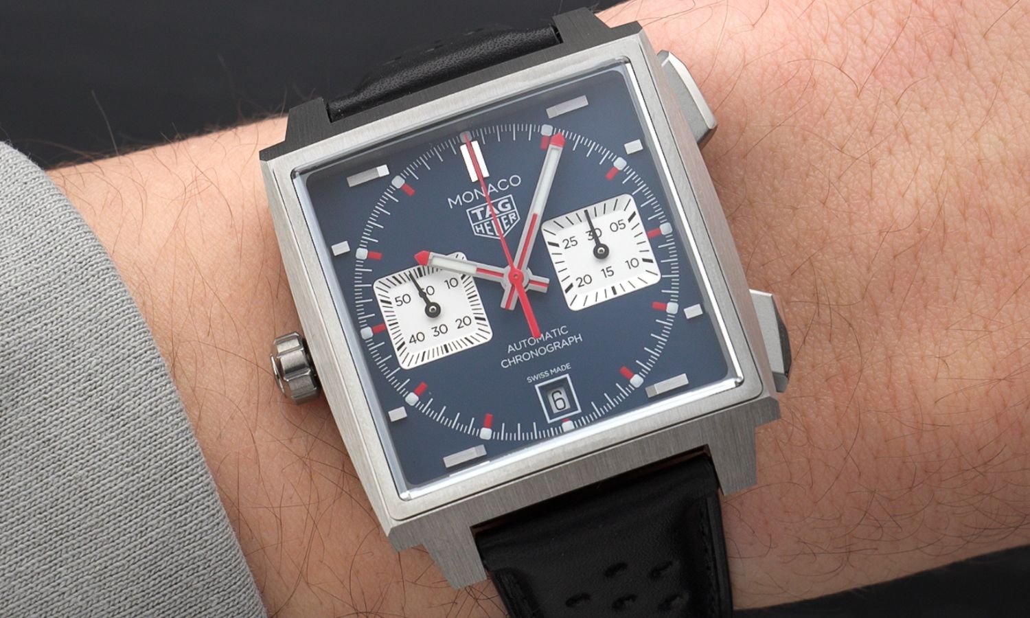 TAG Heuer Monaco 2026 Blau CDW2181.FC8360 mit blauem Zifferblatt am schwarzen Lederarmband an einem Handgelenk mit grauem Ärmel getragen